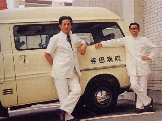 白衣の男性二人と送迎車前  