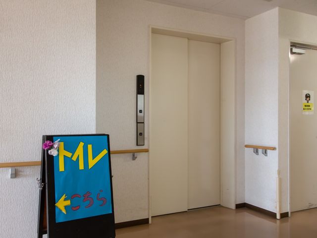 廊下の案内板とエレベーター 表示板  清潔感のある廊下は、案内板も設置されており、目的の場所へのアクセスも容易です。利用者の方々が快適に過ごせる工夫が随所に見受けられます。