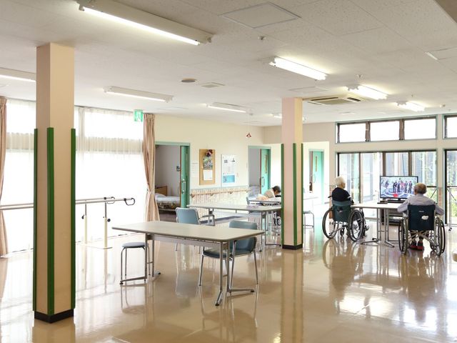 日当たり良好な多目的室 談話室 光が差し込む広々とした空間で、利用者の方々がテレビを視聴されています。交流やリラクゼーションに適した場で活動をサポートできる環境です。