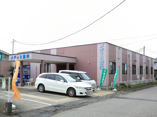 ピンクの外壁の建物エントランス 外観 朱色の看板が目印の開放的なエントランスです。駐車スペースも広々としており、訪れる方を明るく迎えます。