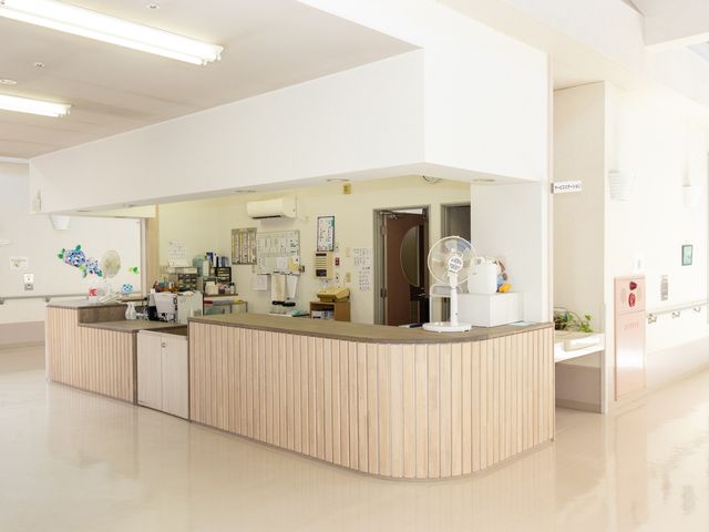 スタッフが働く受付 フロント 清潔感のあるフロントは、自然光が差し込み明るい雰囲気です。スタッフが立ち寄る様子も見られます。