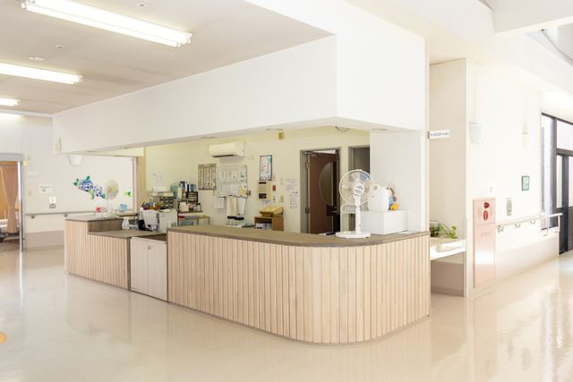 スタッフが働く受付 フロント 清潔感のあるフロントは、自然光が差し込み明るい雰囲気です。スタッフが立ち寄る様子も見られます。