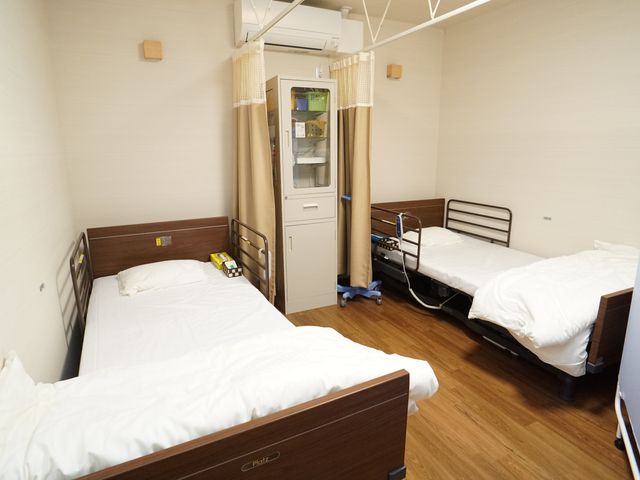 清潔な二人部屋の居室 居室 ゆとりのある空間を持つ二人用の居室です。調整可能なベッドが整えられ、快適な日々を過ごすための配慮が見られます。