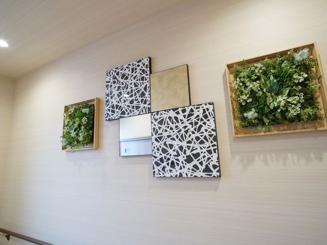 壁面装飾と照明の廊下 展示物 廊下には植物をあしらったアートな装飾が施され、穏やかな光で照らされています。心安らぐ環境でご就業いただけます。