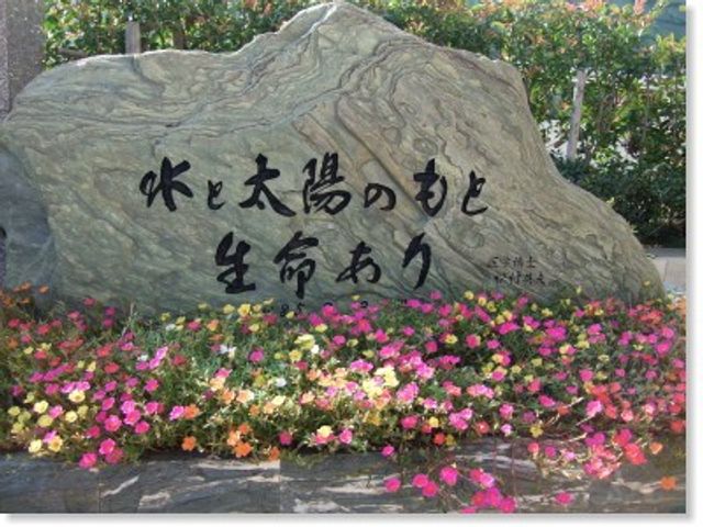 花壇前の看板 外観   花々に囲まれた大きな石の看板があり、落ち着いた印象です。施設の入口まわりの雰囲気を伝えやすい景色です。