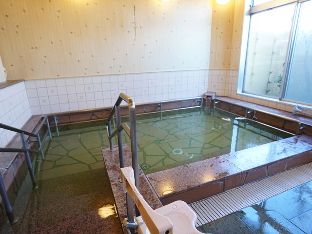 広々とした温泉風呂場 浴室 ゆったりとした造りで、窓から自然光が差し込む浴室です。手すりが設置されており、安全に配慮された空間となっています。