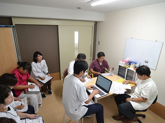 多人数で話し合う会議室 多目的室   職員同士が机を囲み、資料を見ながら打ち合わせをしています。落ち着いた広さの空間で、研修や会議に使いやすそうです。