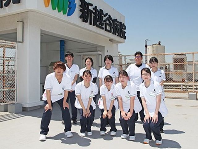 屋上で並ぶスタッフと建物外観 外観   屋上に立つスタッフの皆さんが並び、明るい空の下で笑顔が見られます。建物の看板も確認でき、開放感のある雰囲気です。