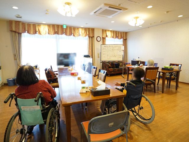 車椅子の方がいる共用スペース 共有スペース 光が差し込む広々としたダイニングで、利用者同士が楽しく過ごしておられます。共有エリアでのコミュニケーションは仕事のやりがいの一つです。