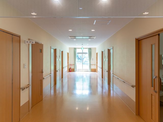 明るい廊下と部屋の扉 廊下 広々とした通路は明るい光が差し込み、清潔感のある落ち着いた雰囲気です。手すりも設けられ安全に配慮が見られます。