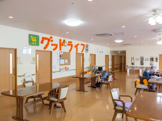 共用スペース活動の風景 リビング ゆったりとした食堂では、住まう方々が様々な活動やくつろぎのひとときを過ごしています。木のテーブルが温かみを感じさせ、アットホームな雰囲気が漂っています。