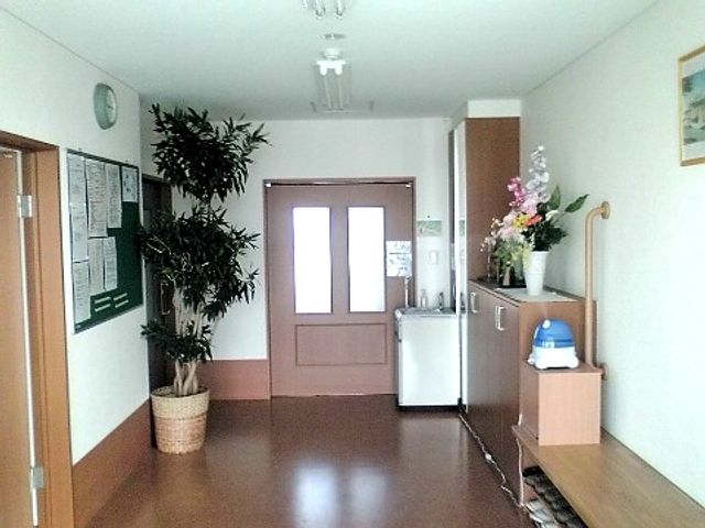 廊下に花と掲示板 エントランス2 開放的なデザインの廊下です。そこには観葉植物と一緒に季節の花が飾られ、心地よい雰囲気を演出しています。