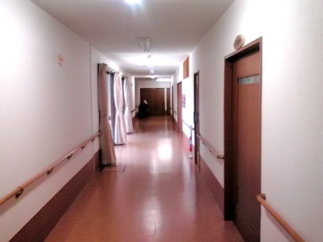 廊下の手摺り付き通路 廊下 手すりが設置された安全を配慮した廊下です。廊下の奥に人がいる様子があり、活動的な雰囲気を感じさせます。