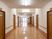 サムネイル 施設の写真 通路幅のある廊下。落ち着いたブラウン色のフローリングで壁紙は白い。両サイドに木製の手すりが設置されている。