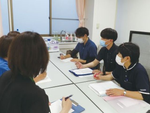 会議中のスタッフ 多目的室   スタッフの方々がテーブルを囲み、メモを取りながら打ち合わせをしています。落ち着いた空間で情報共有しやすい様子です。