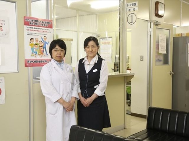 職員が並ぶ受付前 ロビー   受付前で職員の方が並んで立っており、来訪者への案内がしやすい印象です。明るい待合スペースで、落ち着いて応対できそうです。