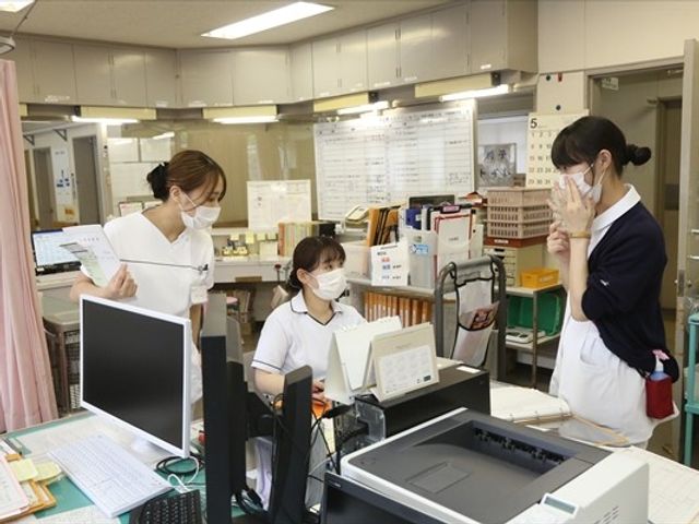 スタッフ3人の受付 フロント   受付でスタッフ同士が打ち合わせをしている様子です。利用者対応の流れが見え、職場の連携をイメージしやすい空間です。