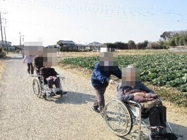 車椅子での散歩風景 レクリエーション 暖かな日差しのもと、職員が利用者様の外出をサポートしています。
