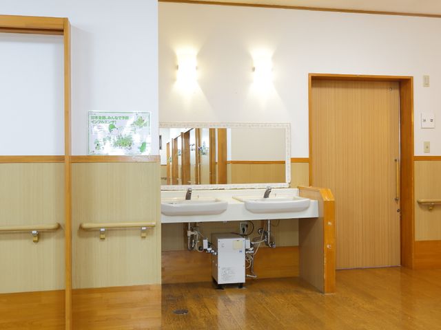 洗面台のある清潔な廊下 洗面スペース 手すりと段差のない床で安全に配慮された洗面スペースです。職員と利用者様の円滑なコミュニケーションを支える機能的な設計になっています。