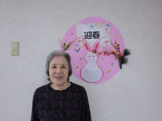 壁飾りの前で微笑む高齢女性