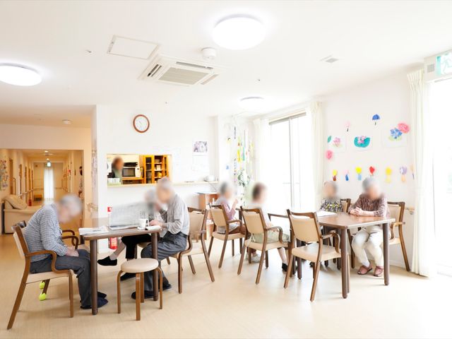 明るい食堂の日常風景 共有スペース 穏やかな光に包まれた食堂で、利用者の方々がお食事や会話を楽しまれています。交流の場としても機能するこの空間は、あたたかな雰囲気です。
