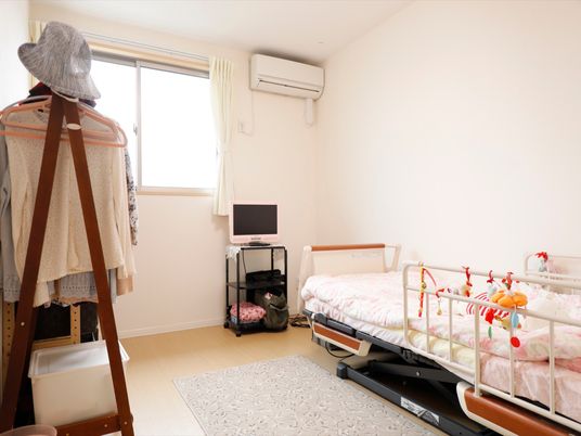 居室には高さが変えられる介護用ベッドが窓際に置かれている。ハンガーラックには衣類がたくさん掛けられている。