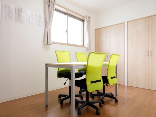 真っ白い部屋で押入れの棚が木目調である。小さな窓の前には、テーブルと黄緑色の椅子が並べられておりとても明るく照らされている。