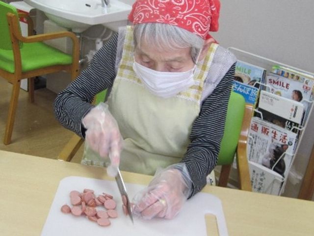 料理活動する高齢者 調理レク 利用者が料理の準備をしている温かな雰囲気の食堂。ここでは自立支援の一環として、日常的な活動を通じたコミュニケーションが育まれています。