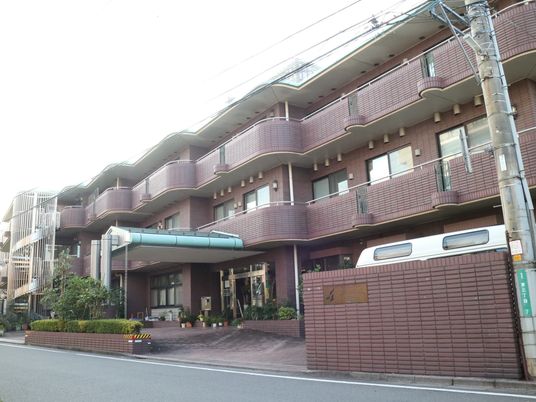 紫色のレンガ柄の外壁の施設である。３階建てで、左奥にらせん状の外階段が見えている。中央に玄関がある。