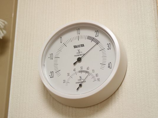 白い壁に温度計がかけられている。白くて丸いデザインで、目盛式のものになっている。温度計の下は湿度計になっている。