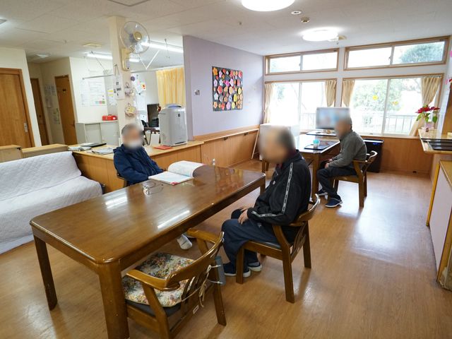 多目的利用の居室 共有スペース 光が差し込む温かみのある居室で、入居者の方々がゆったりと過ごされています。明るい雰囲気の中で、日々の暮らしがサポートされる環境です。