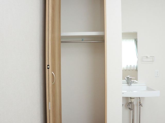 居室のクローゼットと洗面台 クローゼット 木目調のドアが印象的な居室では、清潔感のある洗面台と収納スペースが確保されています。ゆったりとした生活空間が提供される環境が整っております。