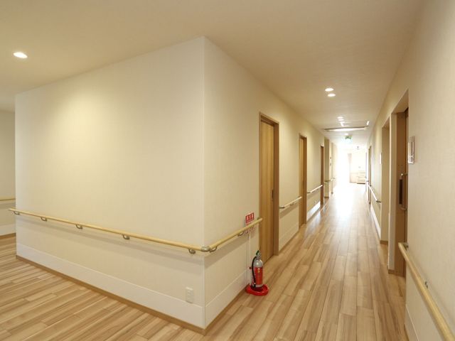 明るい廊下の風景 通路 ゆったりとした廊下は、機能的かつ安全な手すりが設置され、落ち着いた木目調で統一されています。安心してお仕事に専念できる環境が整っております。
