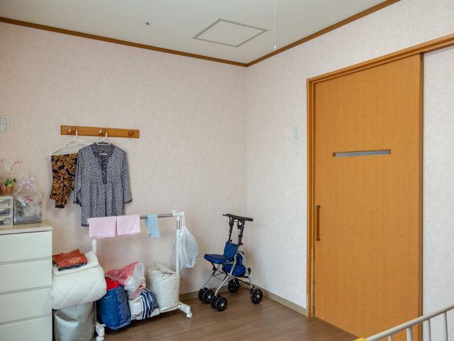 居室の日常風景 居室 ゆとりある居室には日用品を整理する収納スペースがあり、自分らしい空間作りが可能です。壁掛けの服や歩行器も、日々の暮らしを支える大切な一部です。