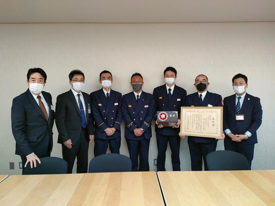 表彰状を持つ人々が並ぶ会議室  