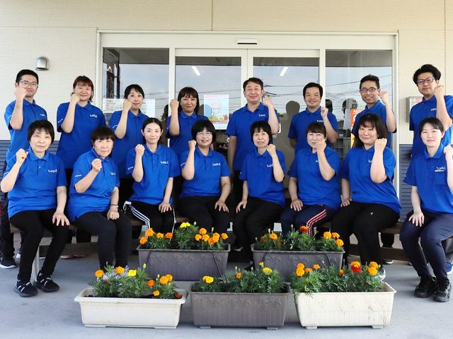 スタッフ集合の笑顔 元気で明るい印象のスタッフが、チームワークを感じさせるポーズで団結しています。職場の雰囲気としては、協力的で和やかな環境がうかがえます。