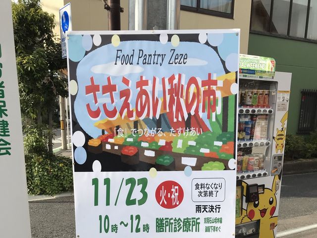 イベント告知の掲示物前 外観   食を通じた交流イベントの案内が掲示され、地域とのつながりを感じられます。自動販売機もあり、施設前の様子が分かります。