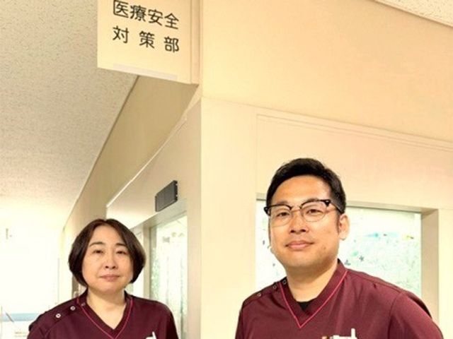 医療安全対策部の入口 廊下   医療安全対策部の案内が見える明るい通路です。スタッフの表情から、落ち着いて働ける雰囲気が伝わります。