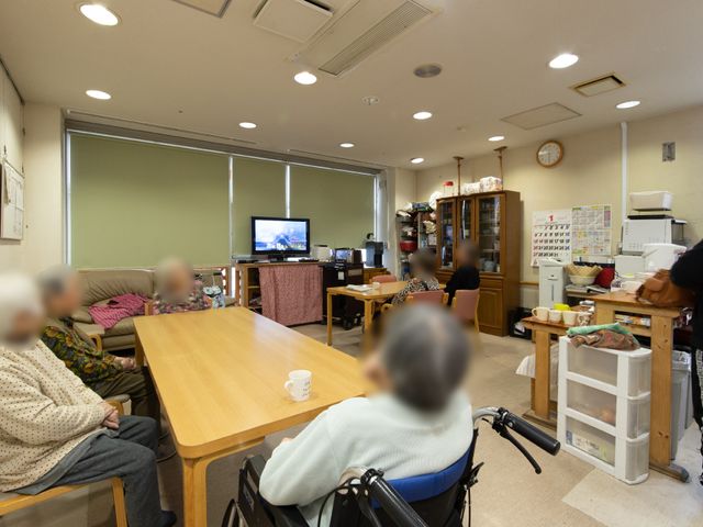 共用スペースで過ごす人々 共有スペース 共用の食堂で、いくつかの椅子に座ってくつろぐ人々が見えます。視聴を楽しんでいる様子や、家庭的な雰囲気が伝わる空間です。