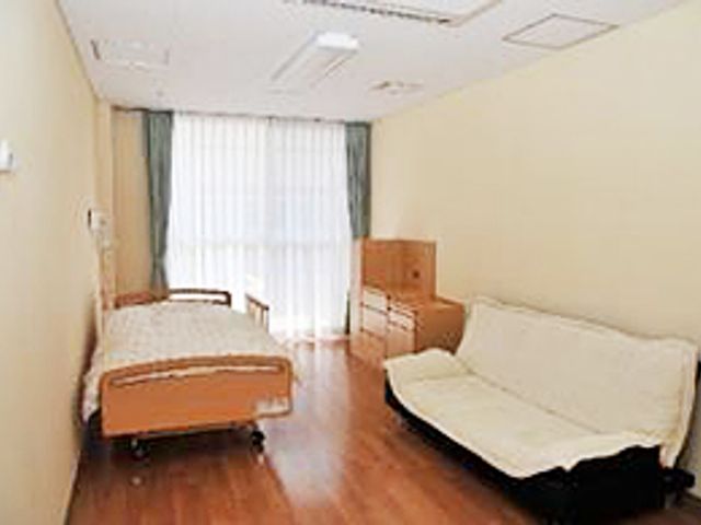 窓際にベッドの居室 居室 窓からの自然光が心地よい居住スペースです。広々とした部屋では、ベッドとソファで快適に過ごせます。