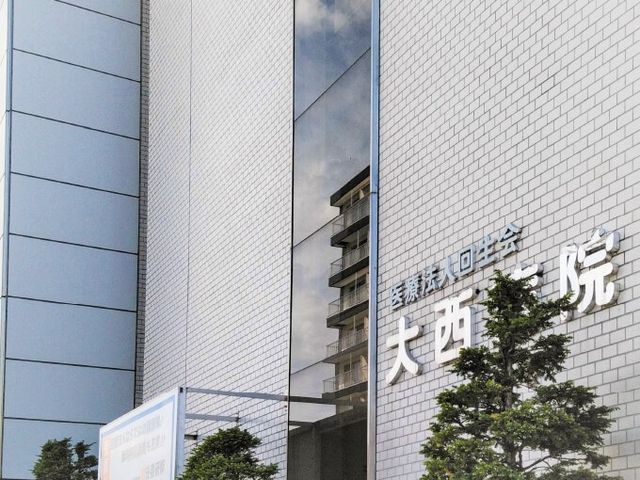 病院名のある建物外観 外観   白い外壁に病院名の看板が掲げられ、窓には周囲の建物が映り込んでいます。落ち着いた印象の建物で、働く場の雰囲気が伝わります。