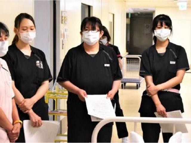 スタッフが並ぶ廊下 廊下   白い手すりのある明るい廊下で、スタッフの方々が書類を手に立っています。就業時の連携や動線の雰囲気が伝わります。