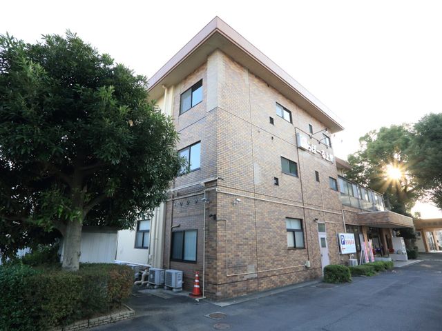 夕日の光る施設外観 外観 夕陽が窓にきらめく落ち着いた色調の建物です。緑豊かな環境が、日々の暮らしに安らぎを与えます。