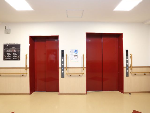 赤いエレベーターのドア エレベーター 床から手すりまでの色分けがされた赤いエレベーターは、必要な情報を記載した掲示物も見やすく設置されており、利便性を追求しています。