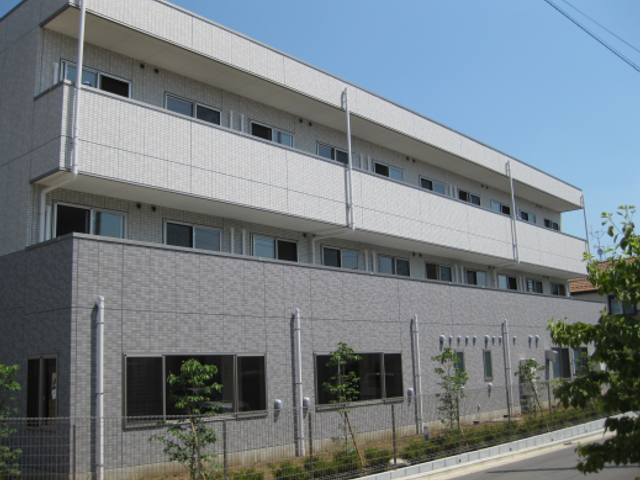 明るい日差しの施設外観 広々とした道路に面した清潔感のある建物です。心地よい環境での就業をお考えの方に適しています。