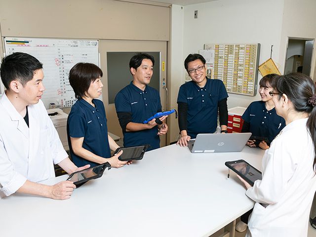 スタッフが会議する居室 スタッフイメージ 笑顔で情報を共有するスタッフたちの様子。日々の運営を支えるチームワークが感じられます。