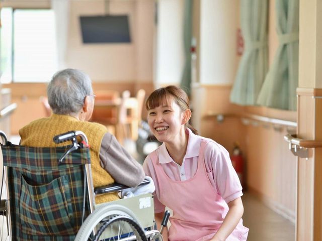 親しみやすい廊下 廊下 明るい廊下で、介護職員が利用者と親しげに会話をしています。温かい雰囲気が感じられます。