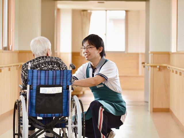笑顔で会話する廊下 廊下 自然光が差し込む明るい廊下で、スタッフが入居者と笑顔で親しく会話しています。