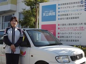 施設前で車に立つ女性と看板の外観  