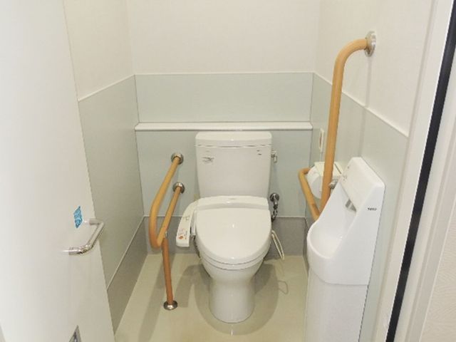 手すり付き個室トイレ トイレ   手すりが複数あり、立ち座りを支えやすいトイレです。清潔感のある明るい空間で、使いやすさが伝わります。